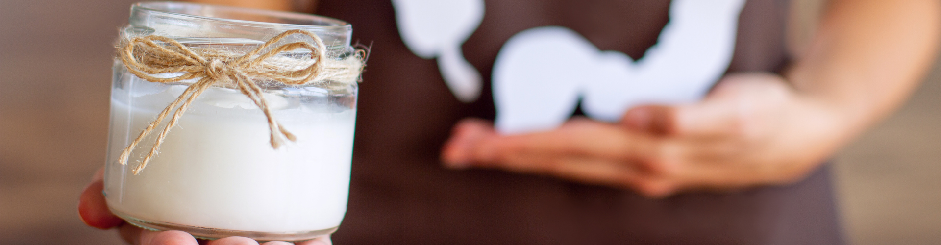 Une jeune femme porte un t-shirt marron avec une impression blanche sur l'intestin. Elle tient dans sa main droite un verre de yogourt. 