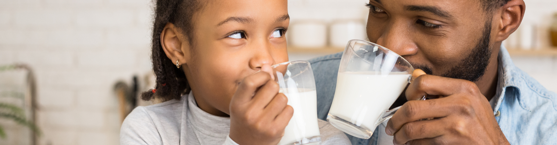 Dans la cuisine, la fille et le père boivent chacun un verre de lait.